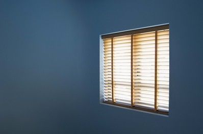 Sunlit home window with wooden blinds against blue wall, interior light control and privacy design.