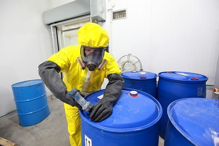 Un hombre con traje amarillo y máscara de gas está trabajando en un barril azul.