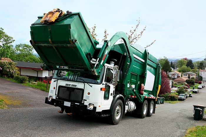 Un camión de basura verde circula por una calle con la tapa abierta.
