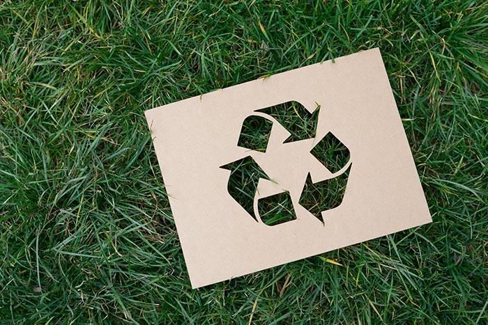 Un trozo de papel con un símbolo de reciclaje recortado está tirado en el césped.