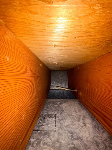 Inside a narrow orange wooden duct or tunnel with a gray floor and ceiling.