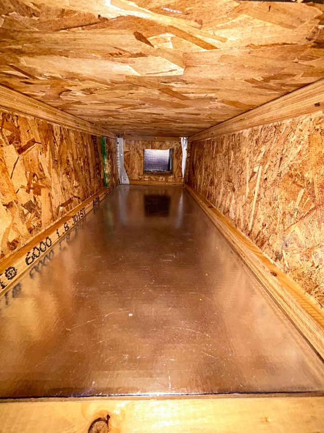 Narrow wooden tunnel or corridor with a smooth floor and a bright opening at the far end