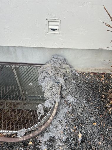 Broken vent and damaged wire mesh with debris piled against a building wall.