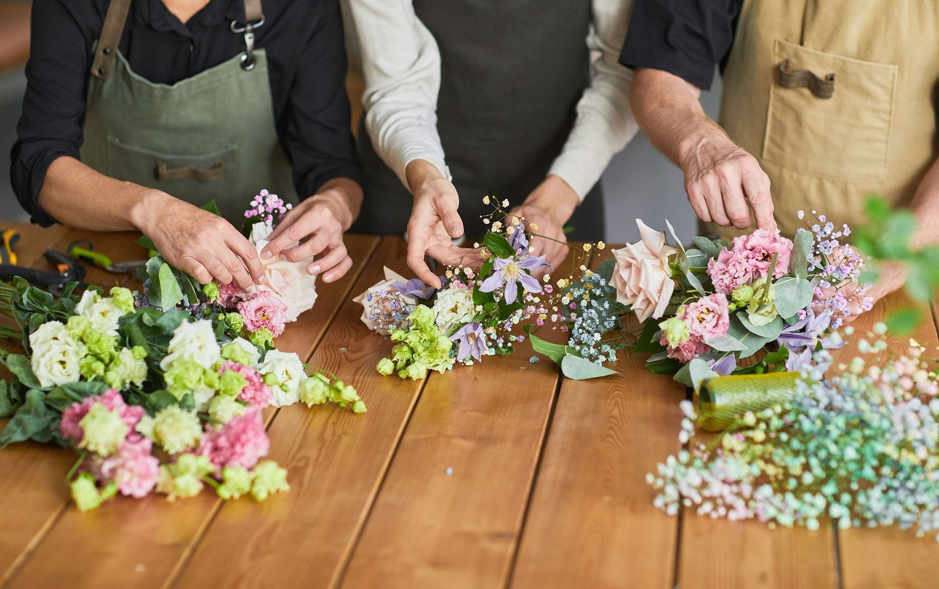 People arranging floral bouquets on a wooden table.