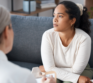 A woman is sitting on a couch talking to a doctor.