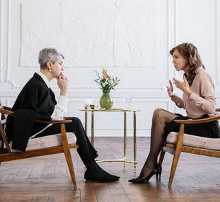 Two women are sitting in chairs talking to each other.