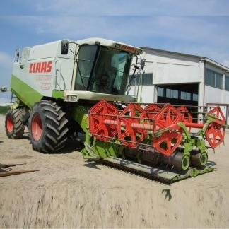 Una mietitrebbia Claas su una superficie sabbiosa di fronte a un edificio bianco in una giornata di sole.