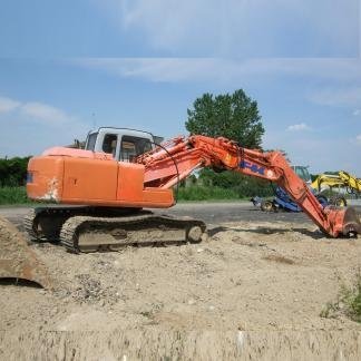 Escavatore Hitachi arancione su una strada sterrata, con braccio teso