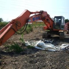 Escavatore Hitachi arancione su una strada sterrata, con braccio teso