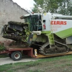 Mietitrebbia Claas su rimorchio. Macchina verde e bianca con cingoli, all'aperto.