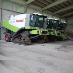 Tre mietitrebbie Claas parcheggiate all'interno di un edificio con pavimento in cemento. 