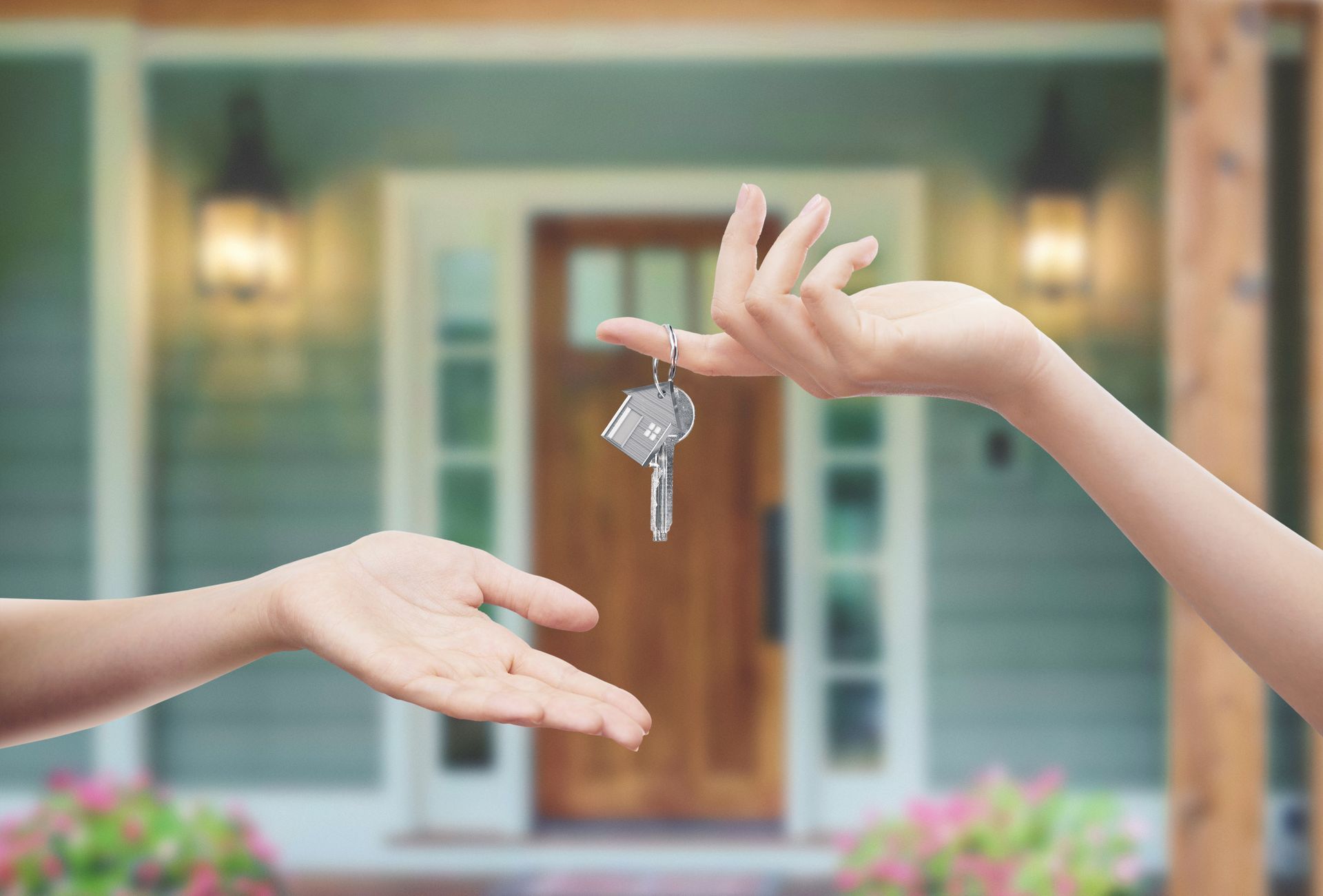 Hands exchanging house keys in front of a blue home porch