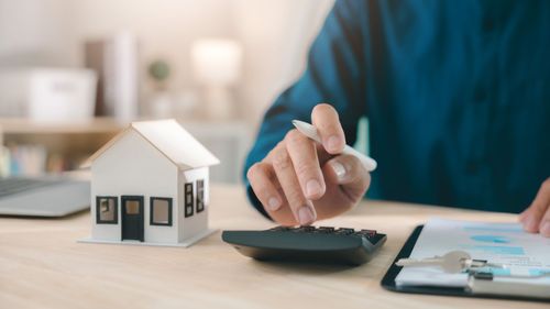Person using calculator beside small house model and paperwork on desk Person using calculator beside small house model and paperwork on desk