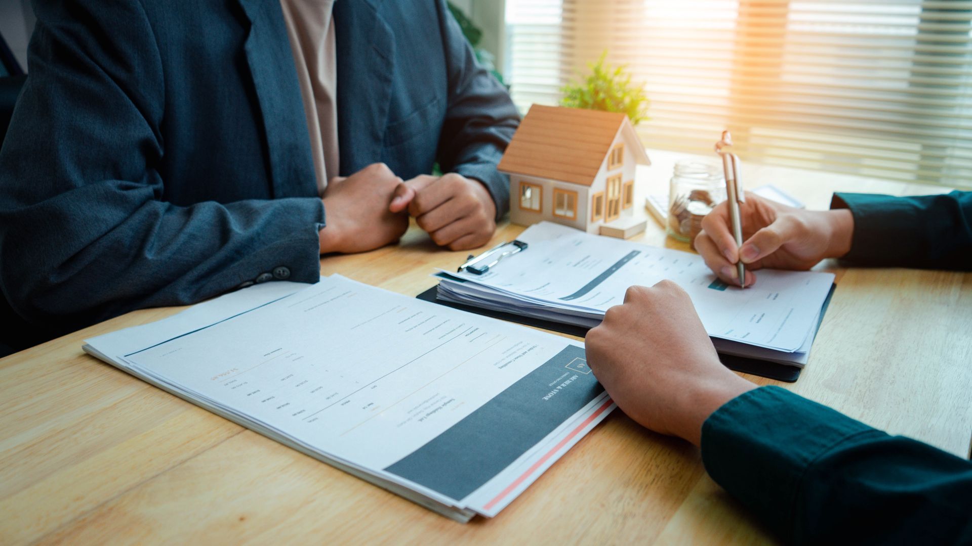 Business meeting with documents being reviewed beside a small house model on a wooden table Business meeting with documents being reviewed beside a small house model on a wooden table