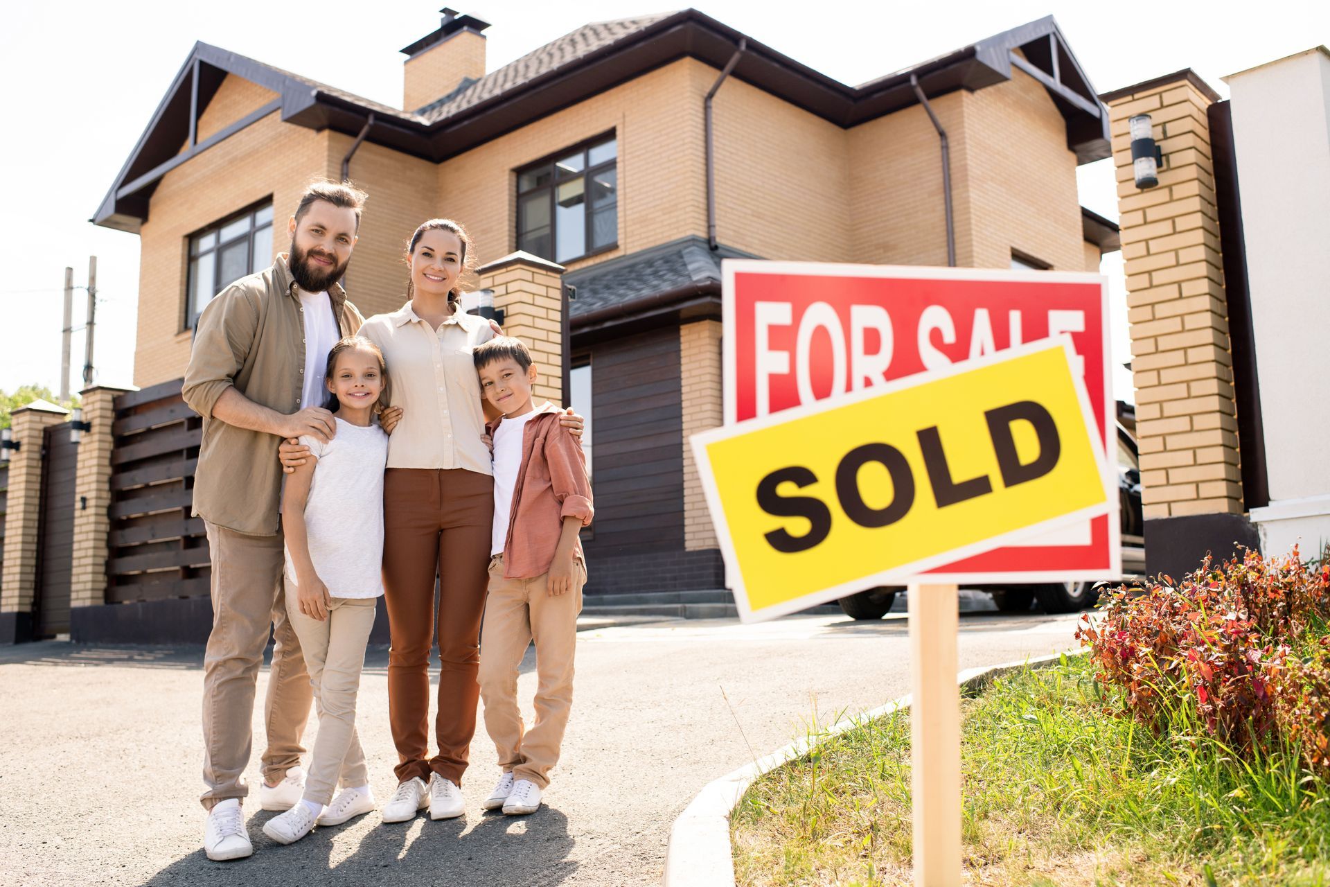 Family standing in front of a house with a red FOR SALE sign and yellow SOLD banner Family standing in front of a house with a red FOR SALE sign and yellow SOLD banner