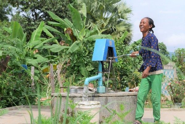 A woman is standing next to a well with water coming out of it.