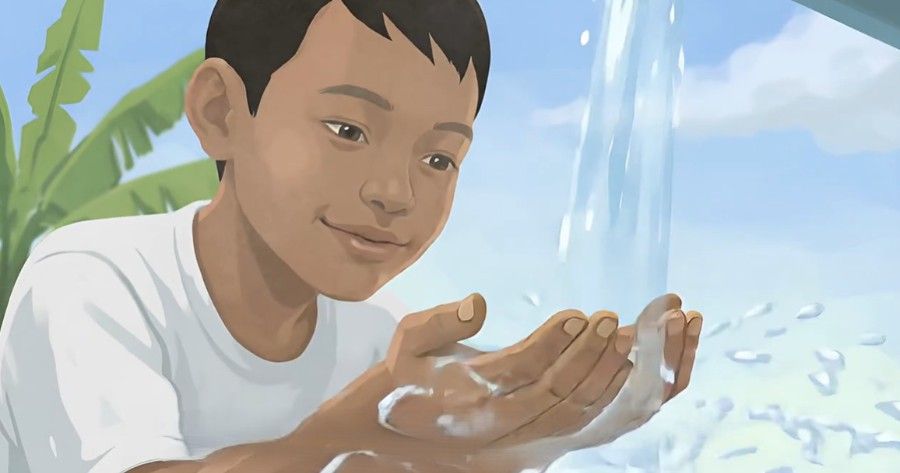 Child cupping water in hands beside a flowing stream, looking at the water with a calm smile