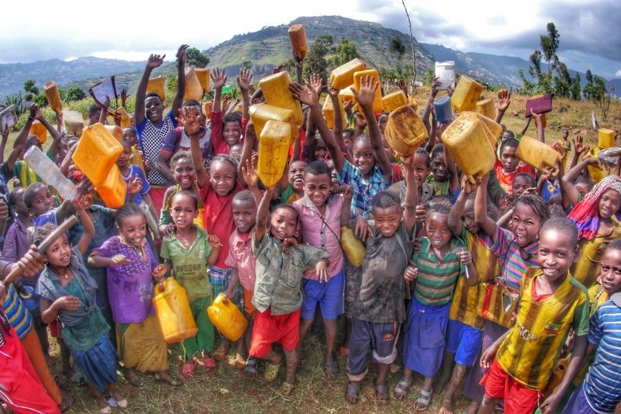 A large group of Ethiopian children are standing in a field holding buckets in their hands.