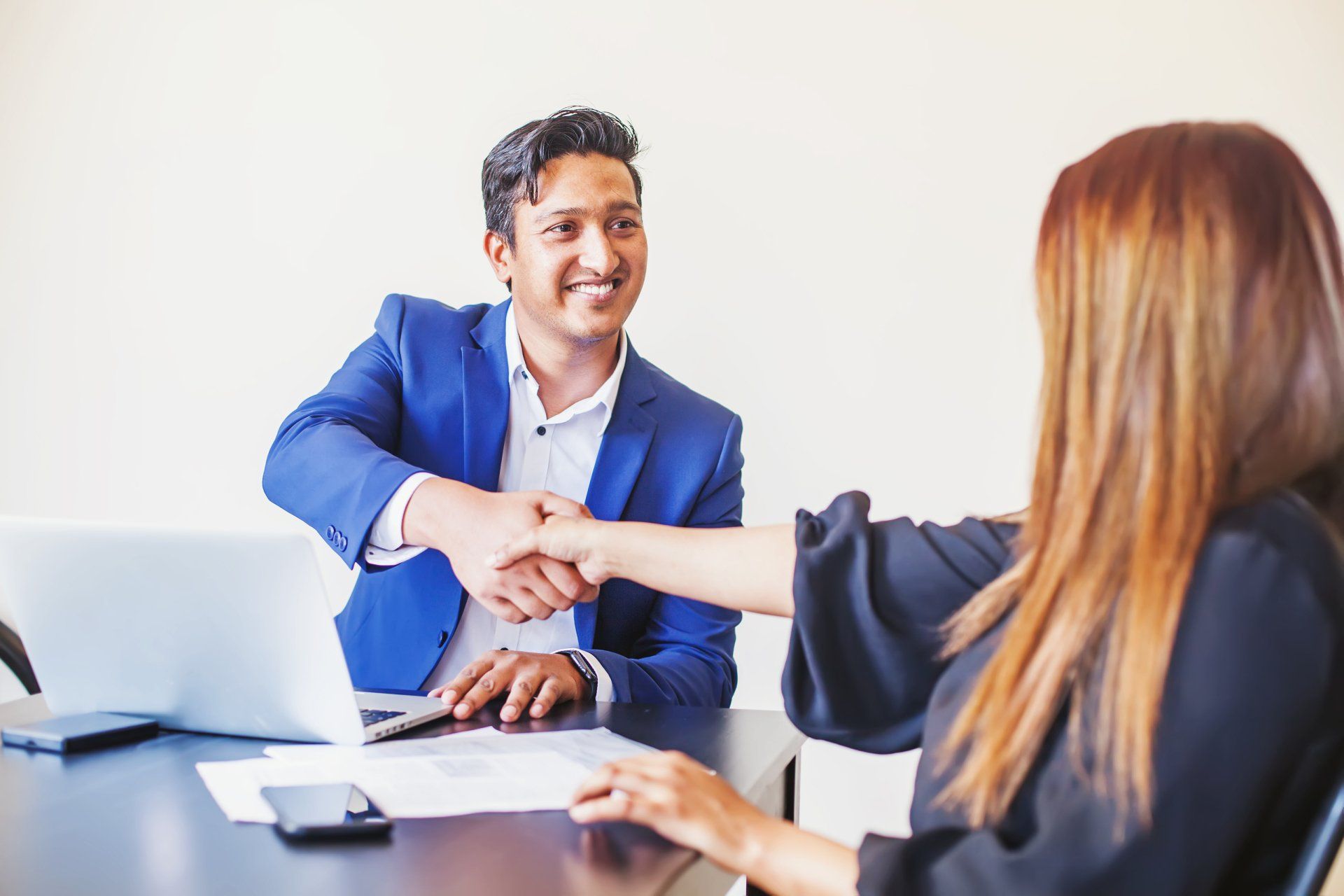 A man in a bright blue suit shakes the hand of a woman with brown hair