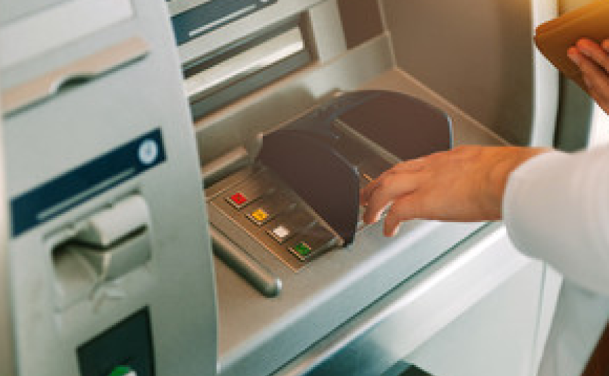 A person's hands reaching toward the keypad of an ATM