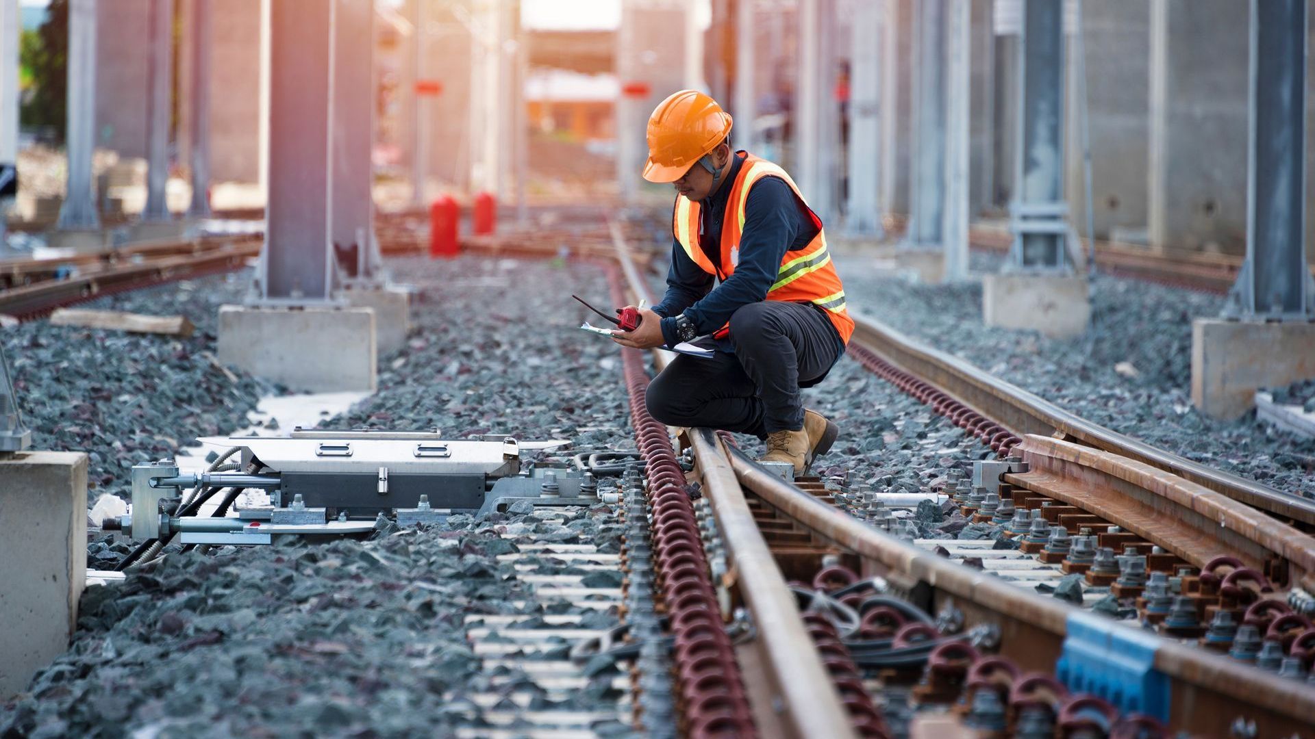 Man in hard hat and high visibility vest crosses by railway track and inspects it.