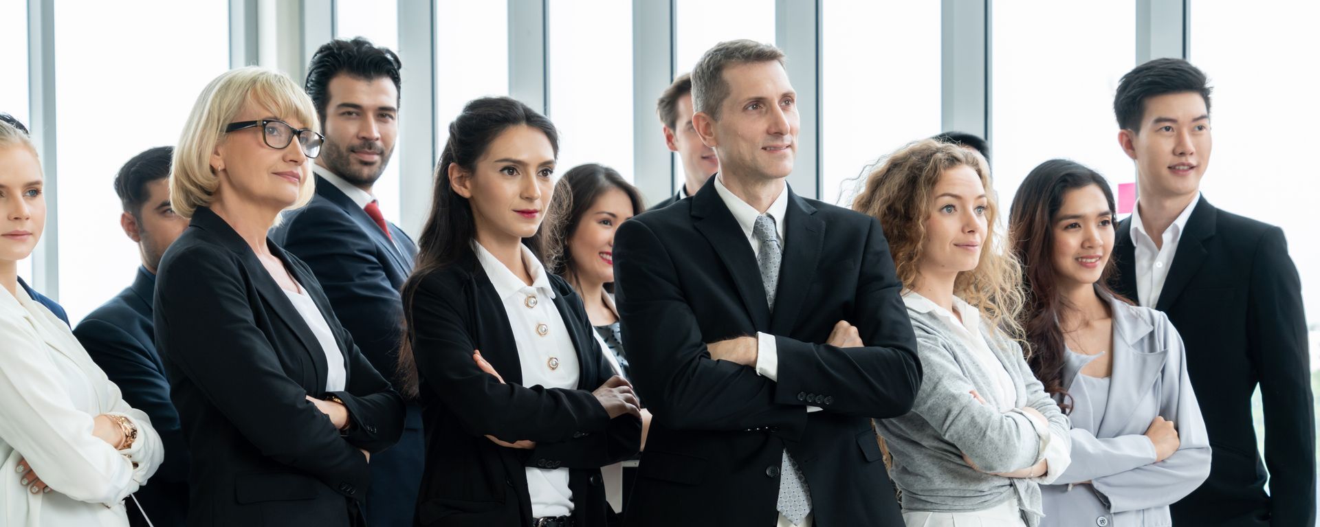 A group of business people are standing in a row with their arms crossed.