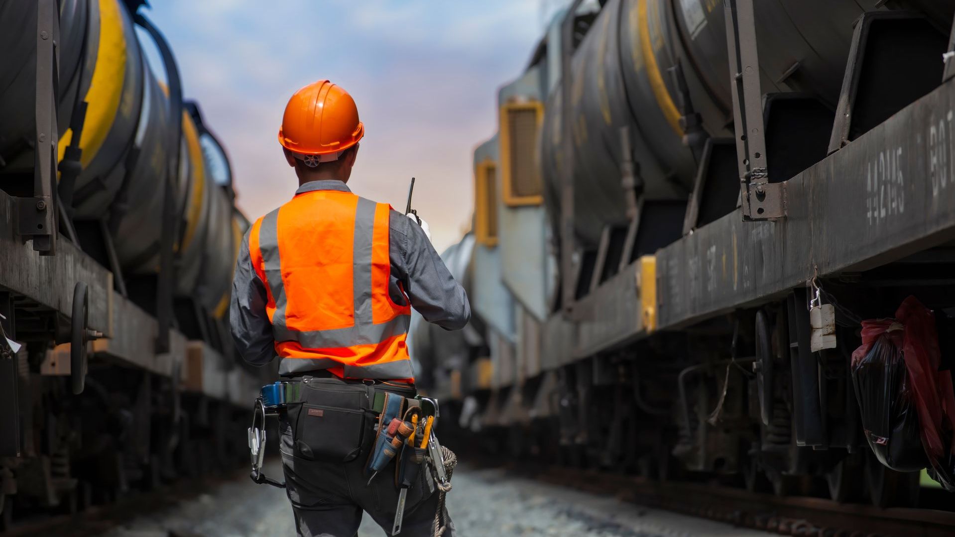 A man with a hard hat and high visibility shirt stands between 2 trains