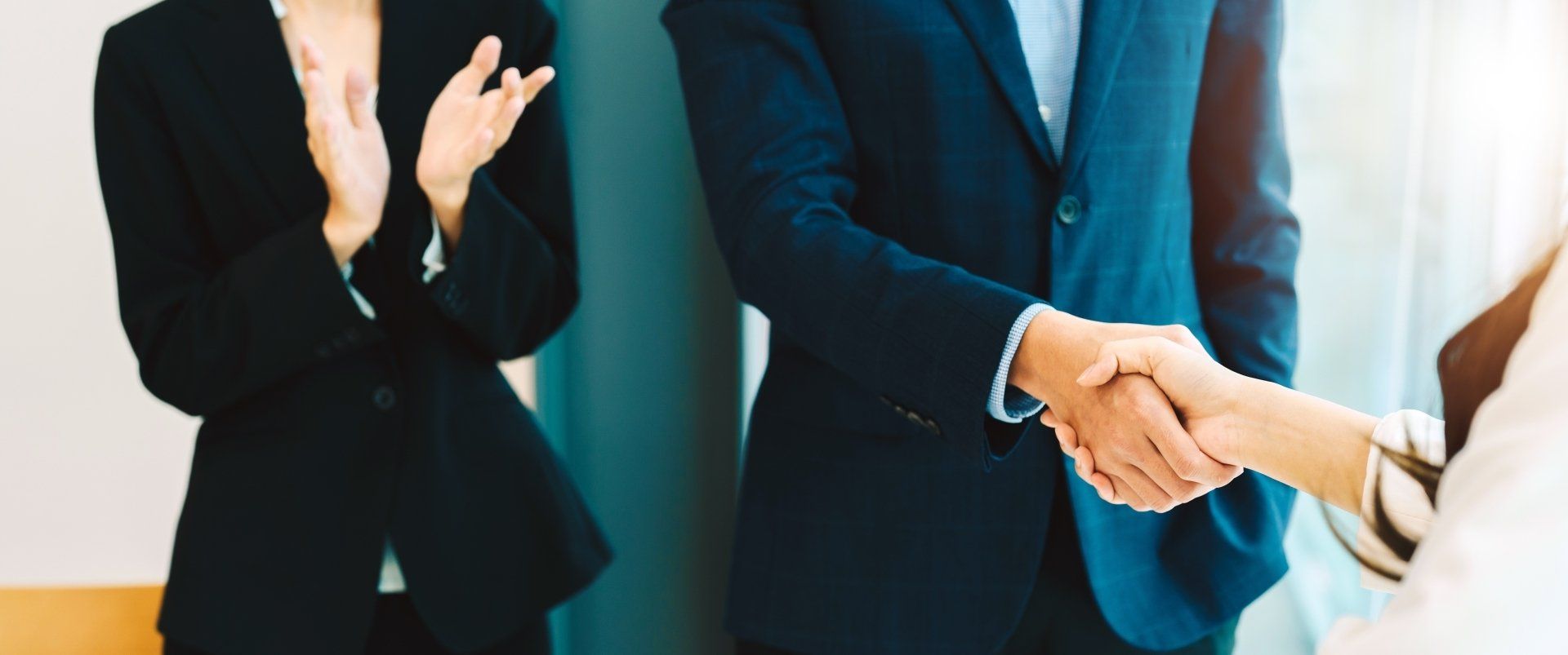 A woman claps as 2 other people shake hands