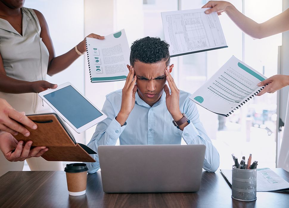 A man is sitting at a desk with a laptop and papers flying around him.