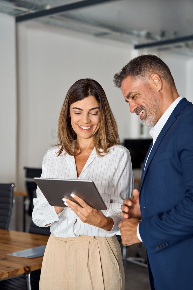 A man and a woman are looking at a tablet together in an office.