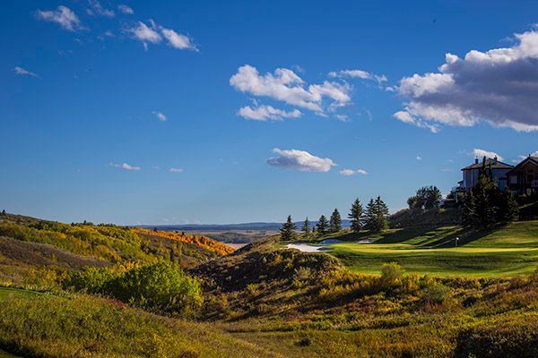 Rolling green hills and golf course under a blue sky with fluffy white clouds.