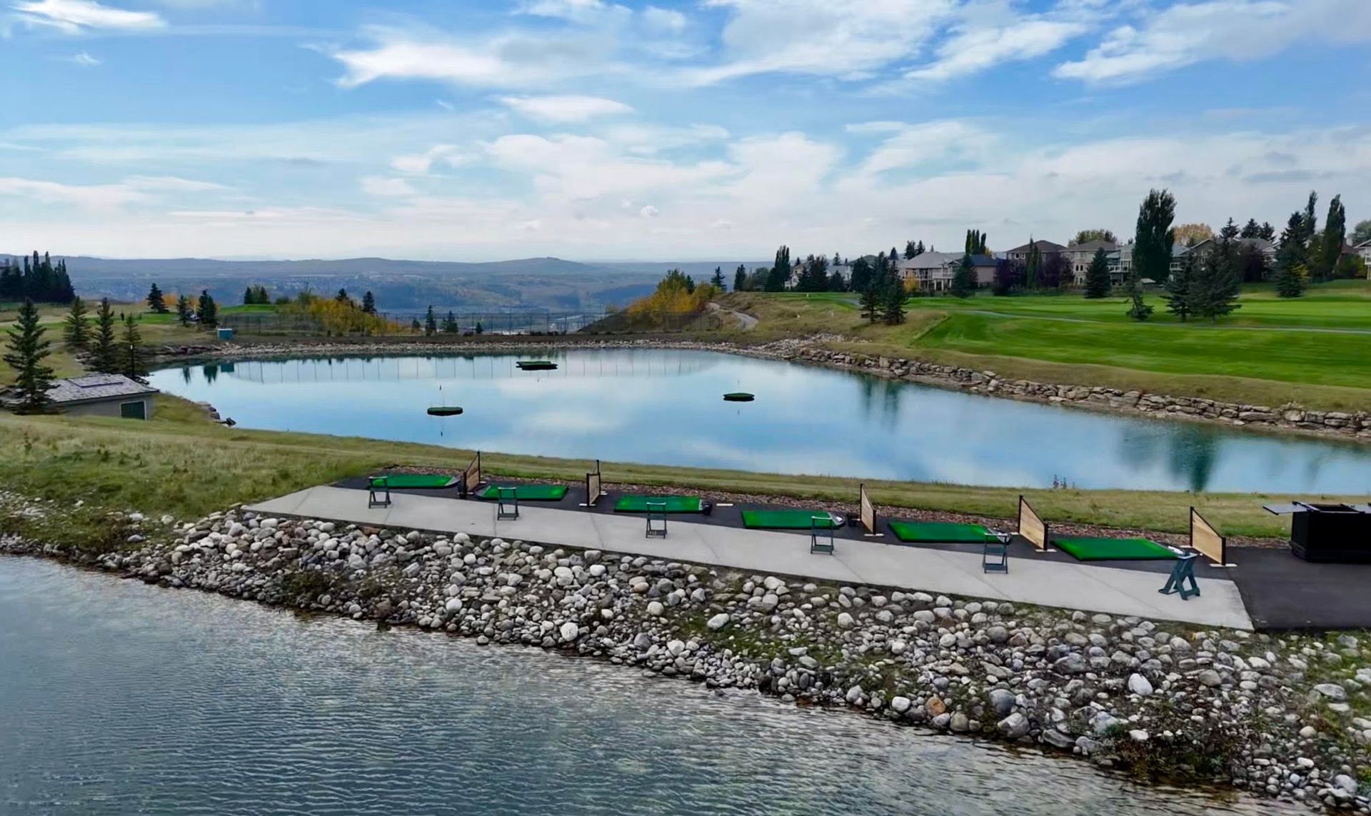Rolling green hills overlook a city and river under a bright, partly cloudy sky; sun shines.