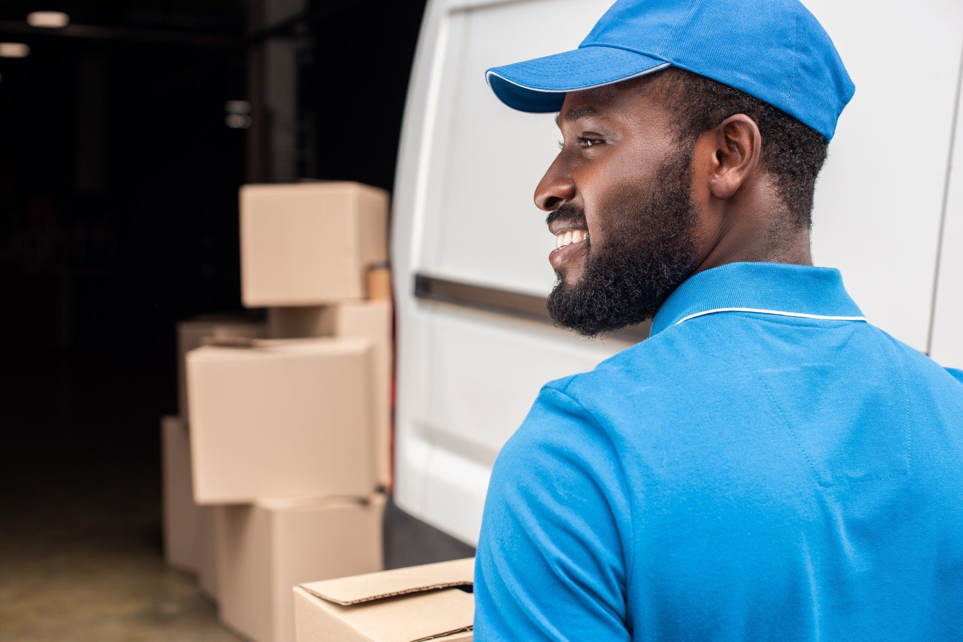 A delivery man is standing in front of a van holding a box.