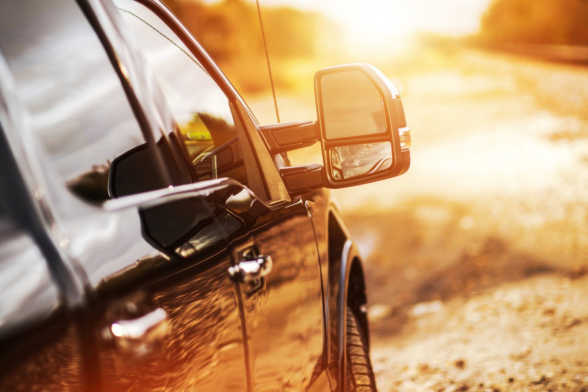 A black truck is parked on the side of a dirt road at sunset.