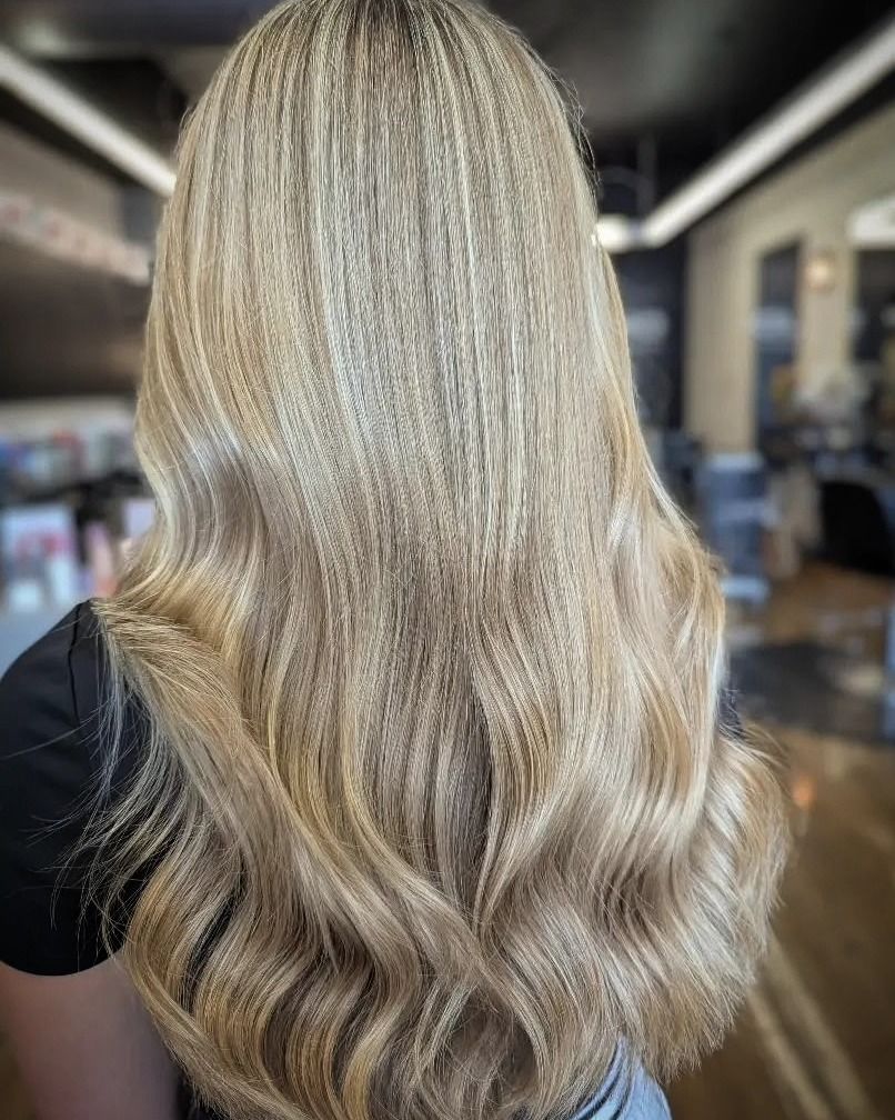Long wavy blonde hair with soft highlights, shown from the back in a salon setting.