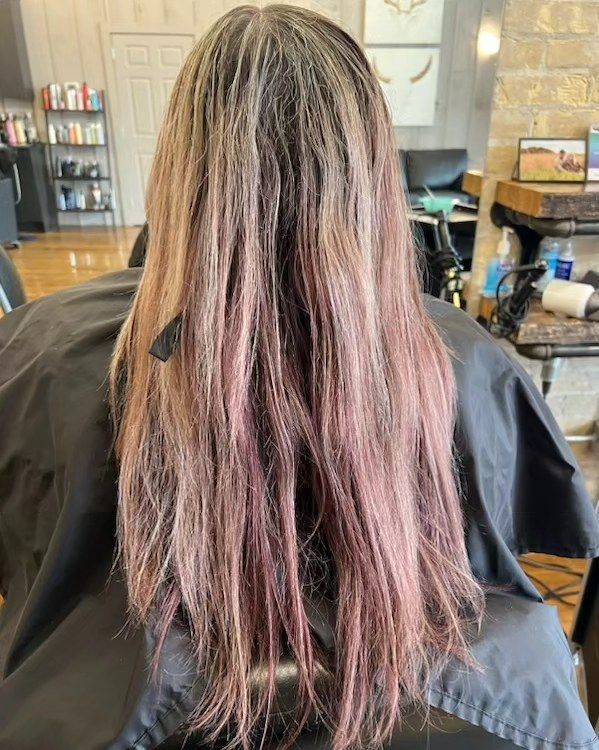 Back view of long, wavy brown hair with faded colour highlights in a salon chair