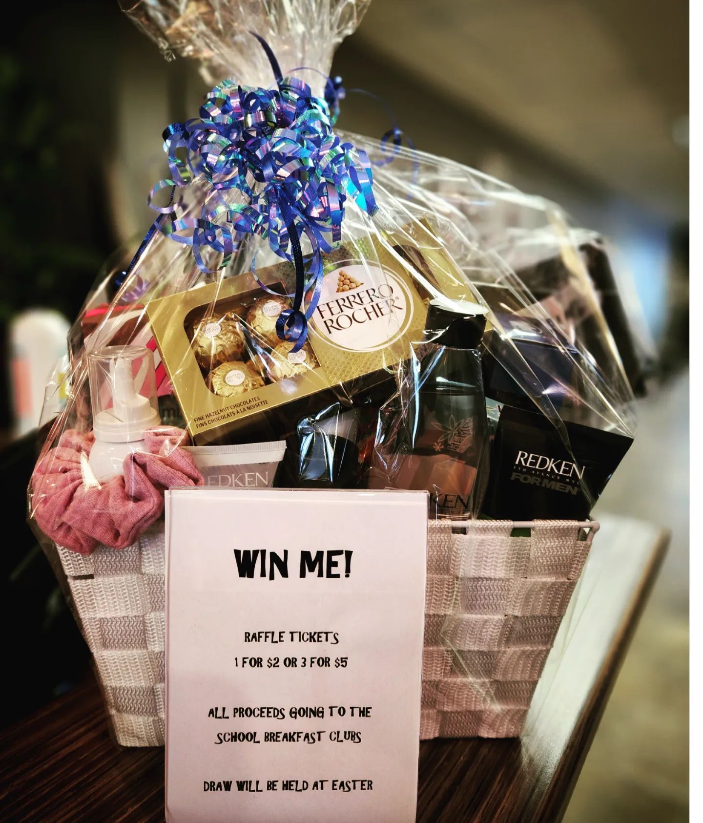Gift basket with assorted treats and a “Win Me!” sign, wrapped in clear cellophane with blue ribbon.