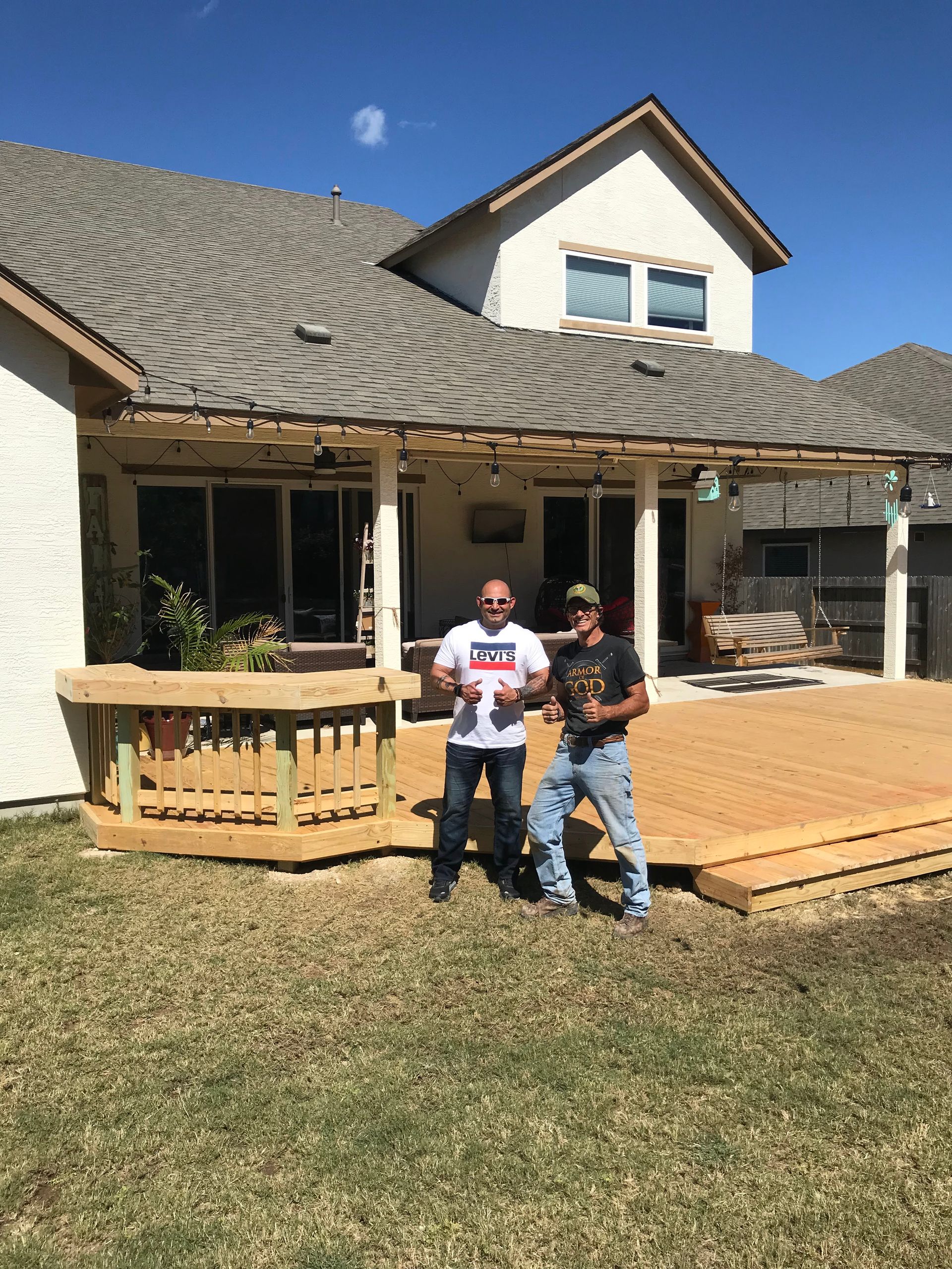 Two men are standing on a wooden deck in front of a house.