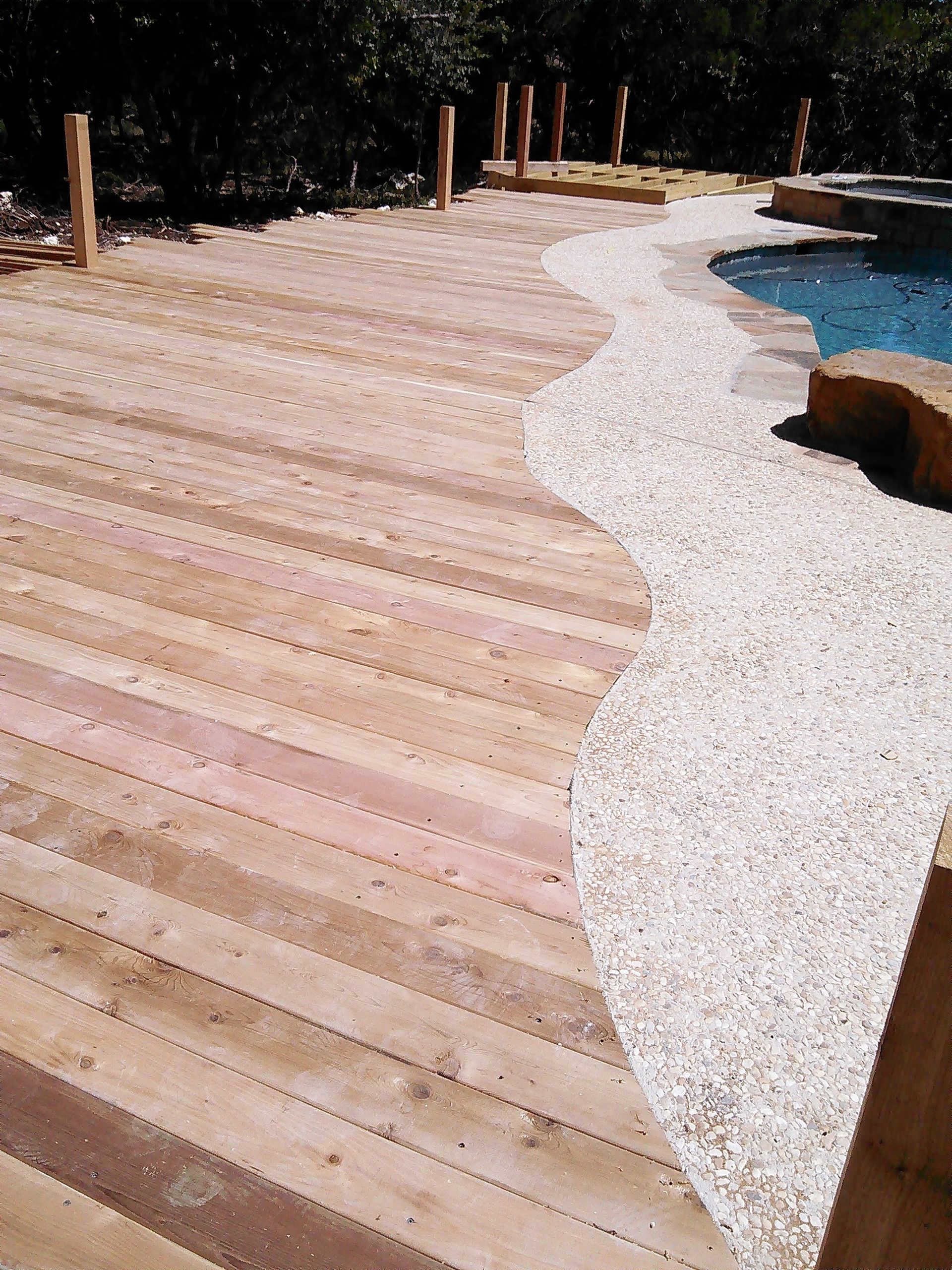 A wooden deck is next to a swimming pool.