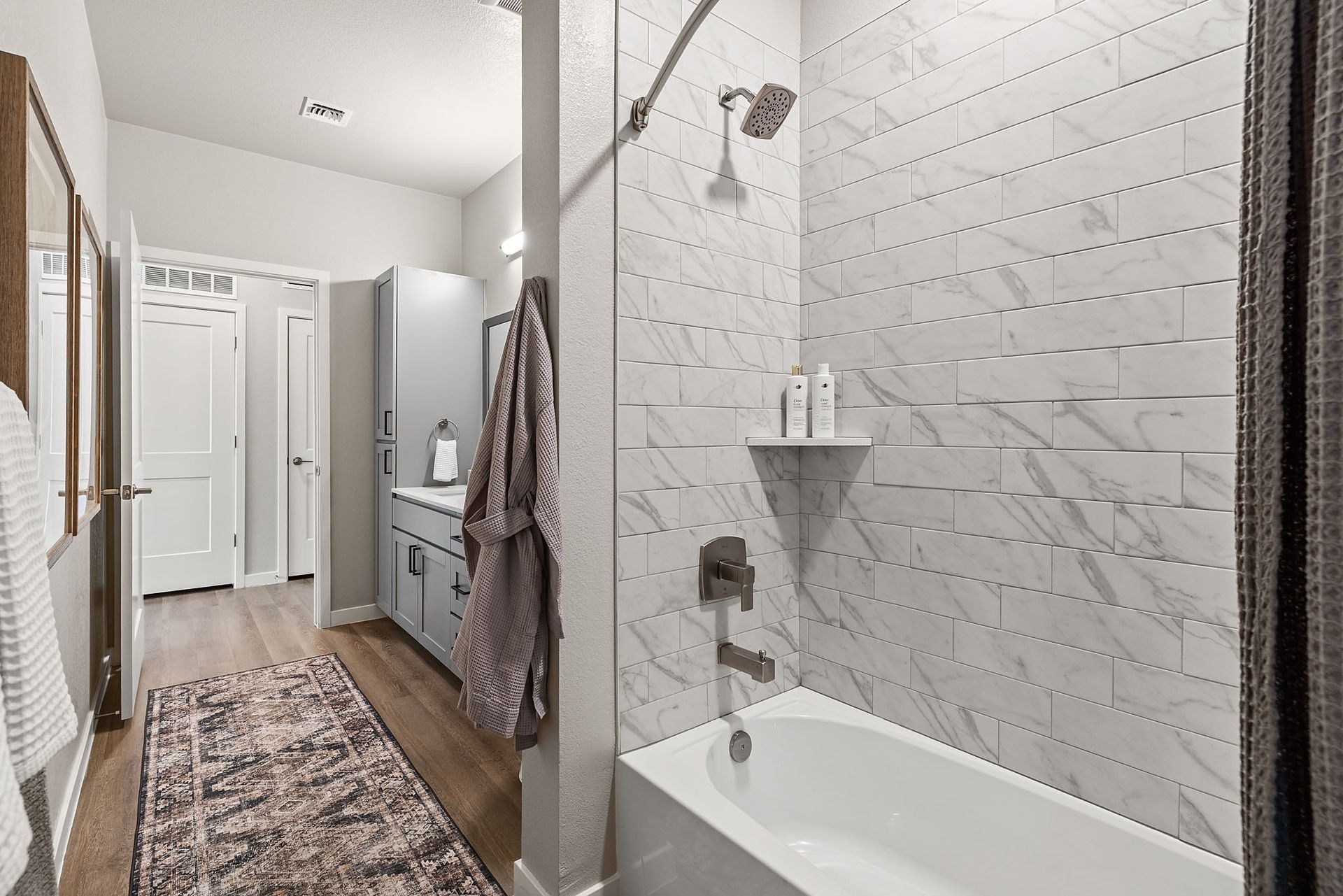 Bathroom with white tile shower, bathtub, vanity, and wood-look flooring at Marq Bronco Butte, offers  1, 2, and 3 bedroom apartments in North Phoenix, AZ. A rug and robe hang inside.