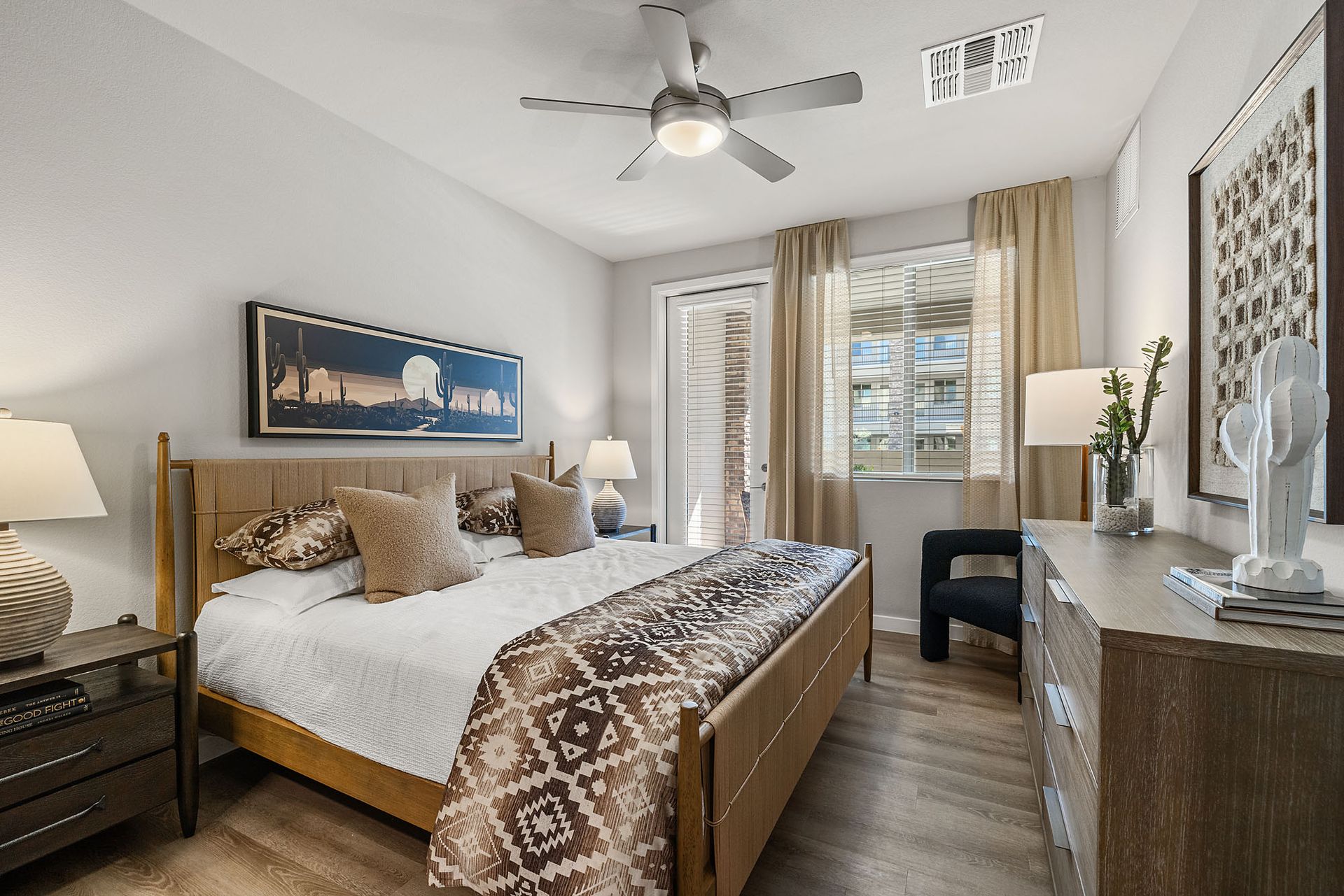 Bedroom with bed, nightstands, dresser, window, and ceiling fan. Warm tones, natural light at Marq Bronco Butte, offers  1, 2, and 3 bedroom apartments in North Phoenix, AZ.