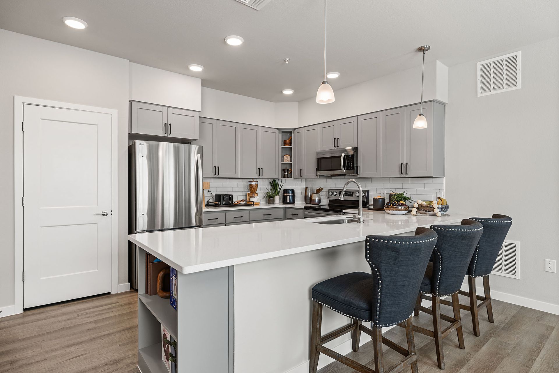 Modern kitchen with gray cabinets, white countertop island, and three blue bar stools at Marq Bronco Butte, offers  apartments in North Phoenix, AZ.