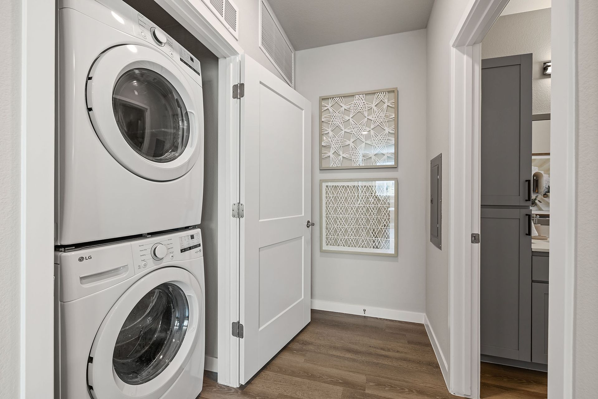 Stacked washer and dryer in a laundry room, next to a closed door and framed artwork at Marq Bronco Butte, offers  1, 2, and 3 bedroom apartments in North Phoenix, AZ.