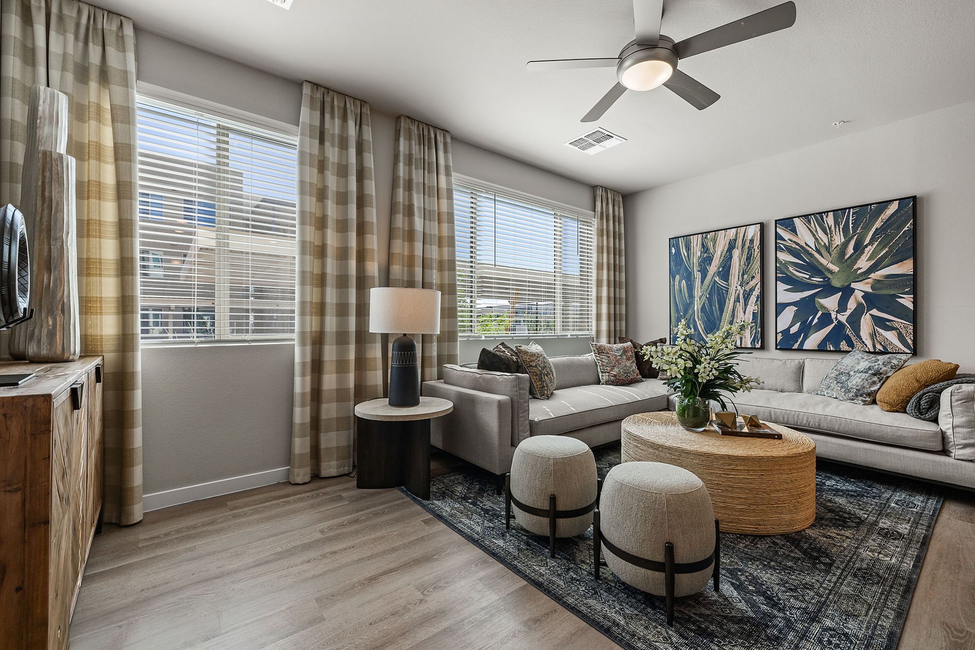 Living room with gray sofa, patterned rug, coffee table, two patterned stools, and windows with plaid curtains at Marq Bronco Butte, offers  apartments in North Phoenix, AZ.