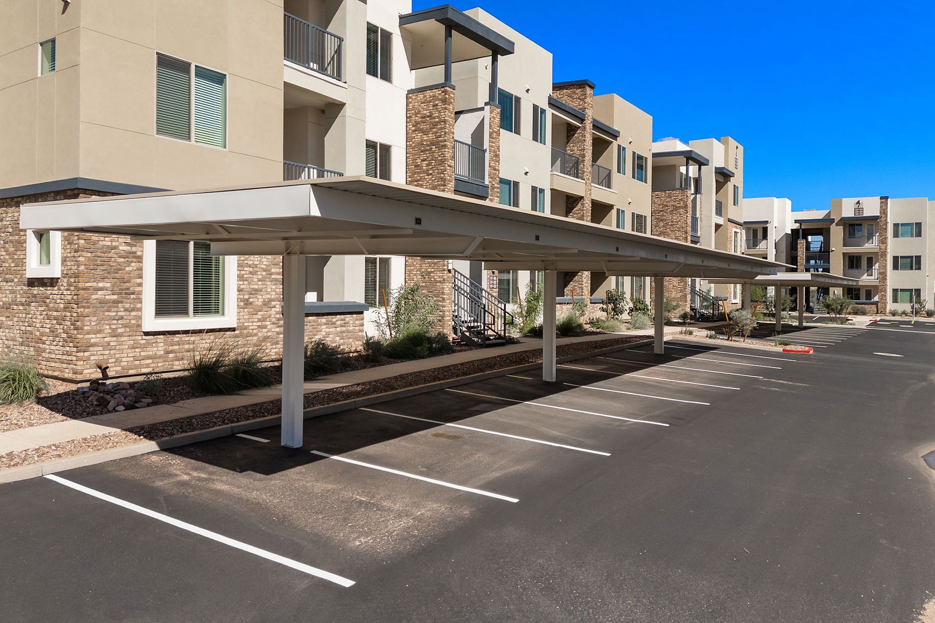 Carport shading parking spaces at a beige apartment building with stone accents at Marq Bronco Butte, offers  1, 2, and 3 bedroom apartments in North Phoenix, AZ.