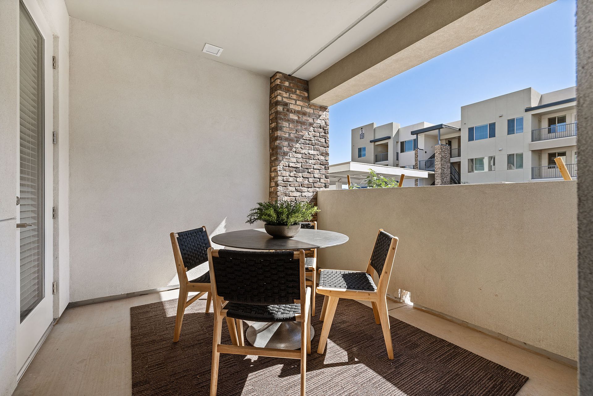 Balcony with table and chairs; view of other buildings at Marq Bronco Butte, offers  1, 2, and 3 bedroom apartments in North Phoenix, AZ, with smart home features. Sunny day, neutral color tones.