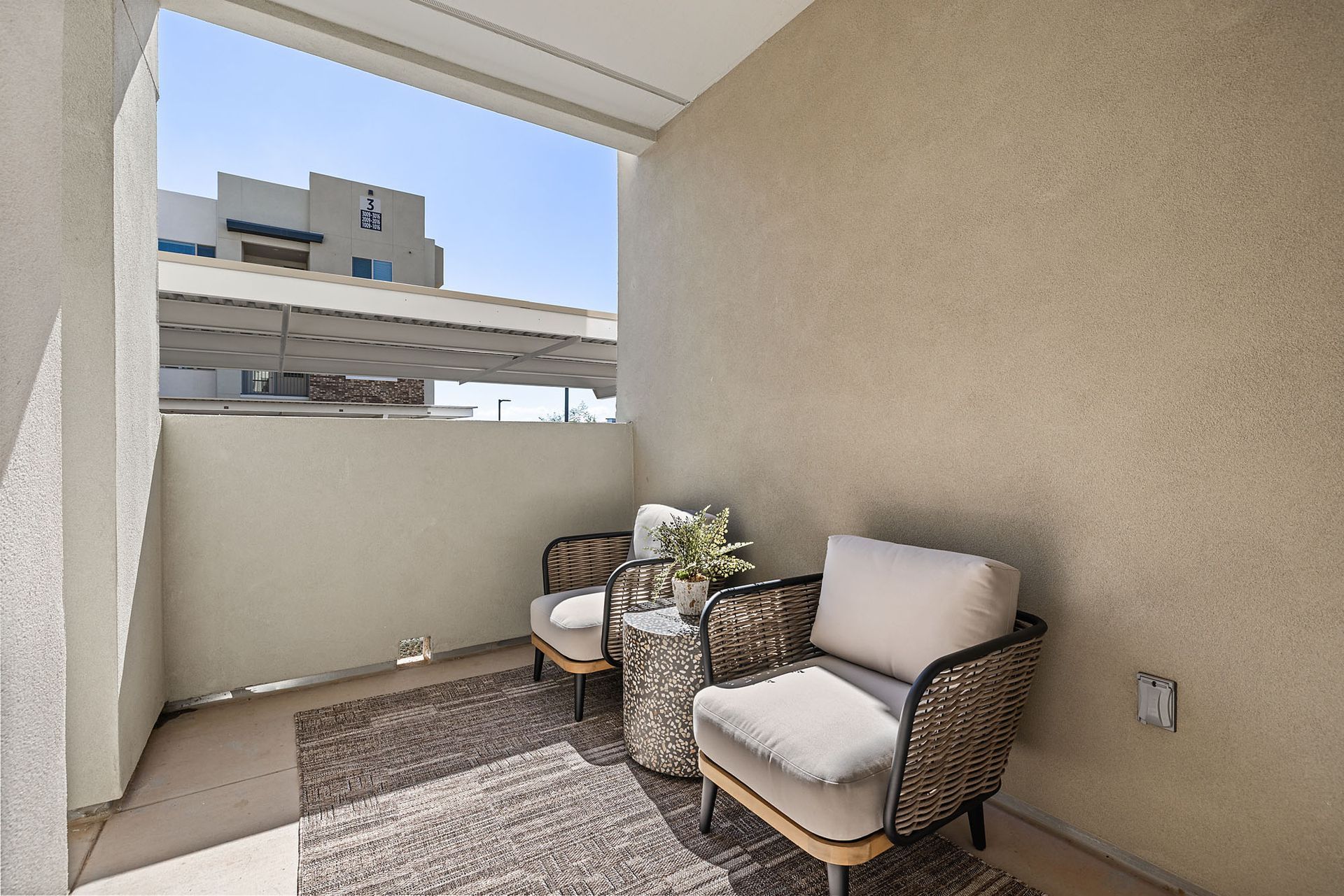 Small balcony with two chairs, a small table, rug, and plants at Marq Bronco Butte, offers  apartments in North Phoenix, AZ. Light beige walls and blue sky.