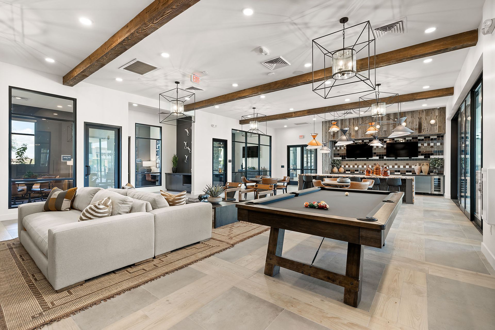 Spacious lounge with pool table, bar area, and large windows at Marq Bronco Butte, offers brand-new apartments in North Phoenix, AZ.  White walls, exposed wooden beams, and neutral-toned furniture.