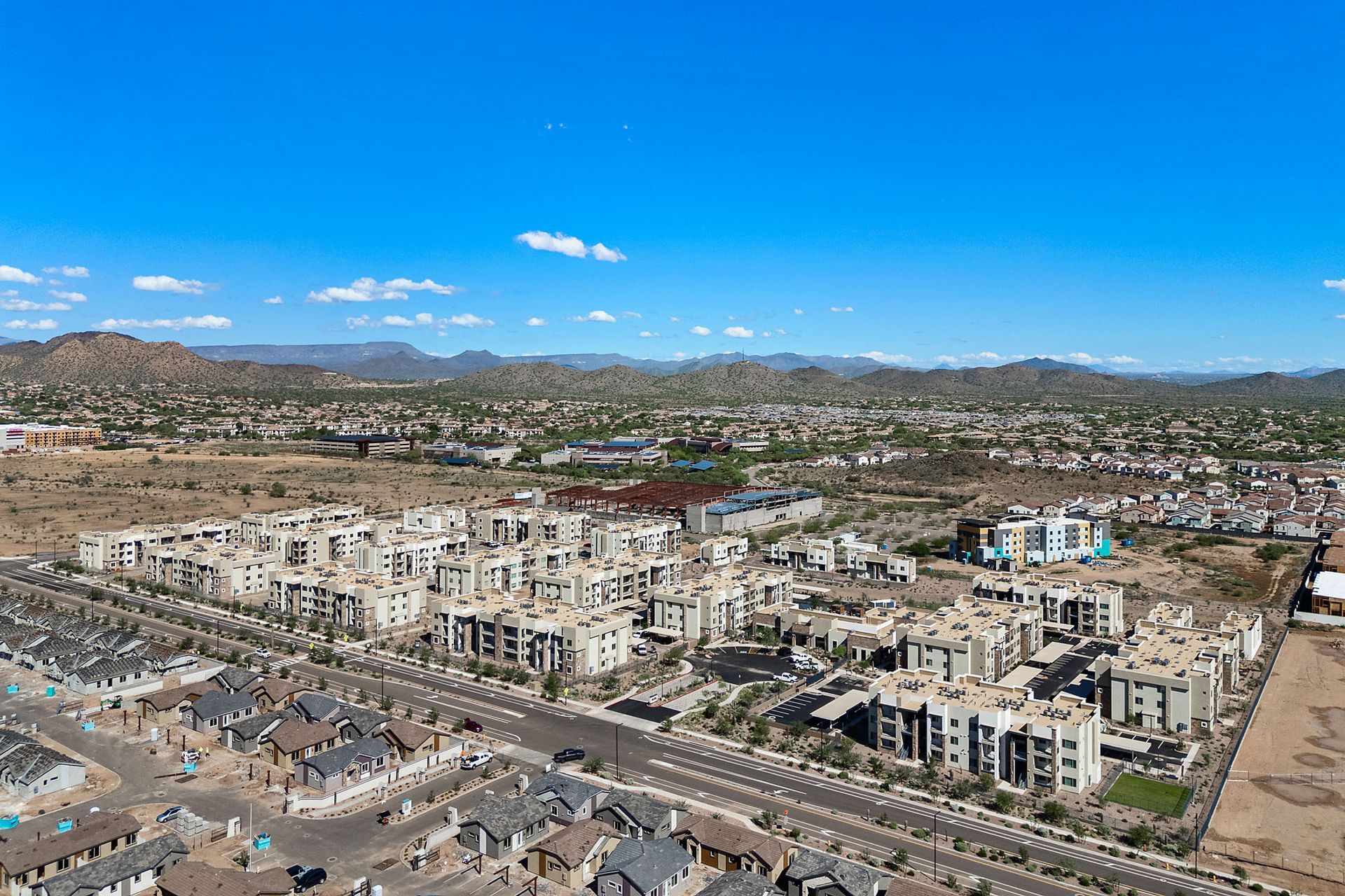 Aerial view of a suburban development with beige buildings, roads, and mountains in the background under a blue sky at Marq Bronco Butte, offers  1, 2, and 3 bedroom apartments in North Valley, Phoenix.