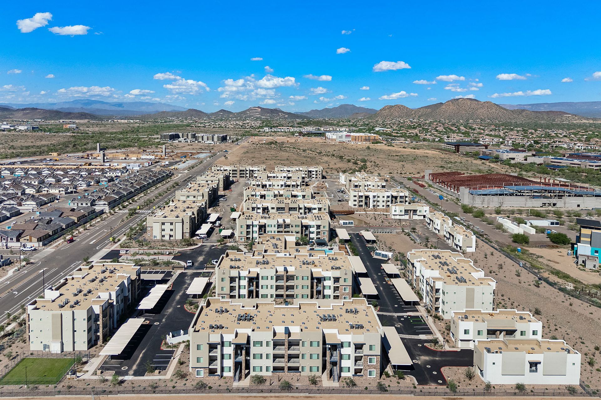Aerial view of apartment buildings in a desert landscape under a blue sky with mountains in the background at Marq Bronco Butte, offers  1, 2, and 3 bedroom apartments in North Phoenix, AZ.